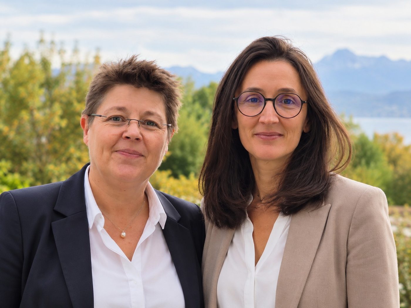 Armelle Hemon-Laurens, à gauche en veste bleue, et Laetitia Chaumont, à droite en veste beige, cofondatrices de Formation Esprit Colibri, devant un paysage de montagnes et de lac.